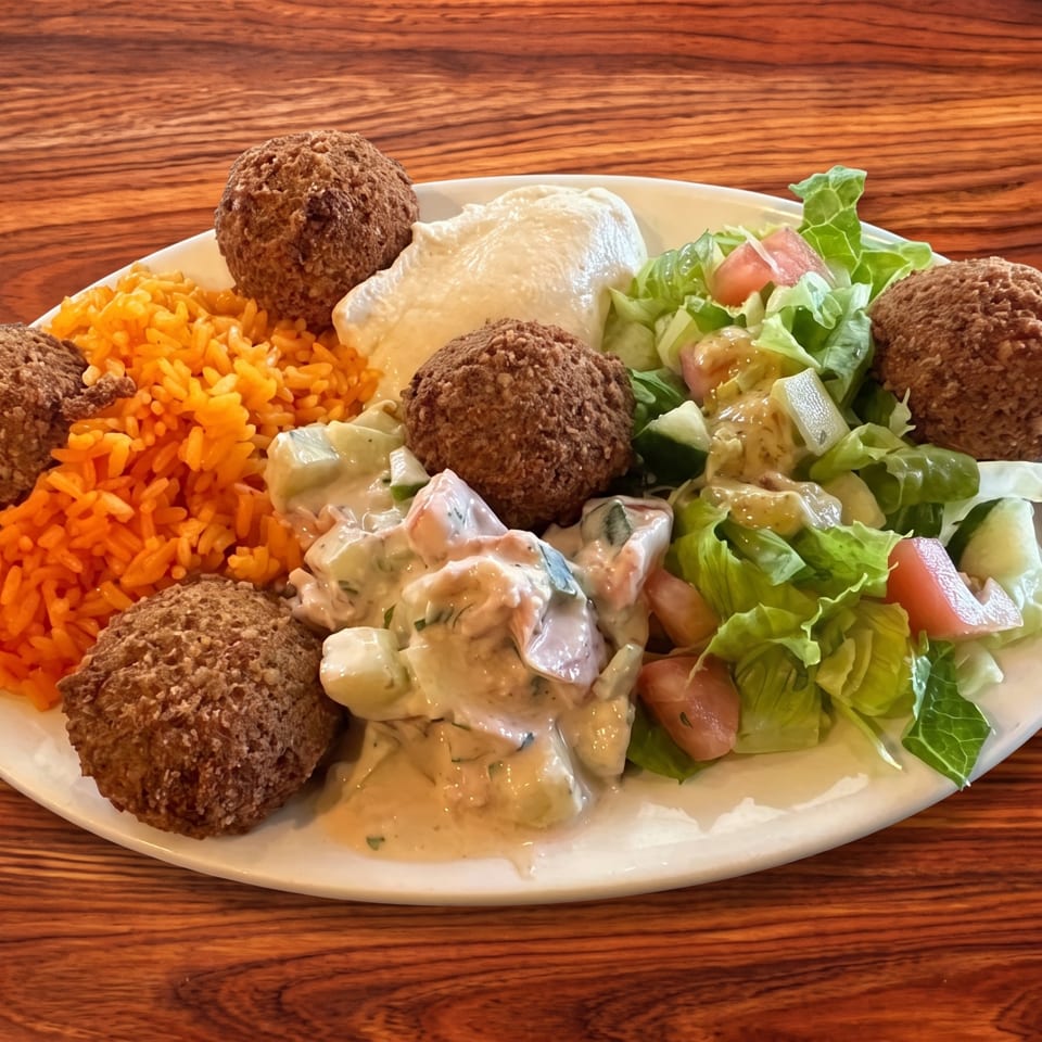 Plate of falafel balls, orange rice, creamy salad, and lettuce salad on a wooden table.