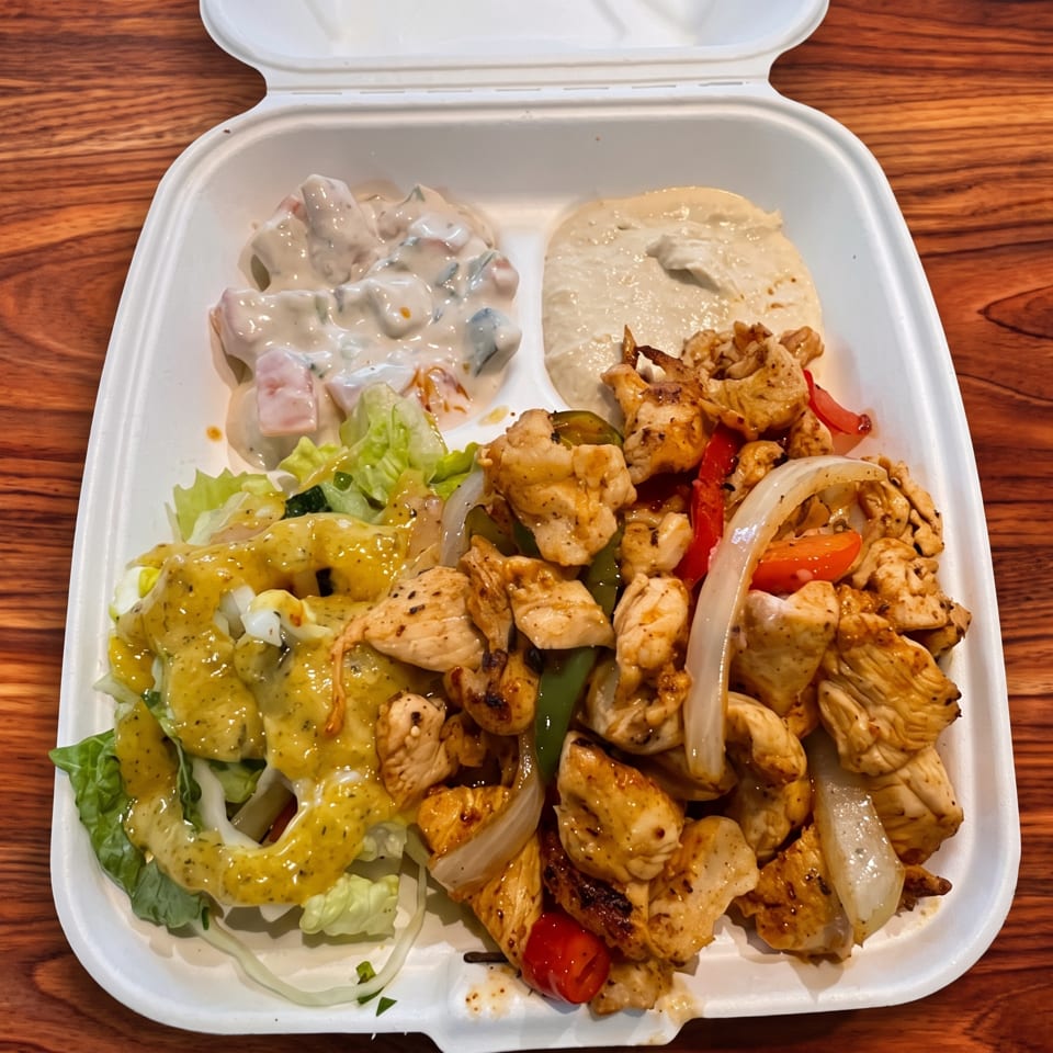Takeout container filled with grilled chicken, sautéed peppers and onions, salad with creamy dressing, and pita bread.